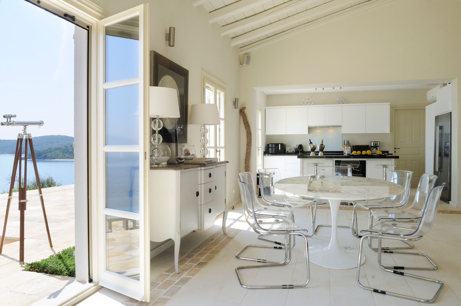 Open plan dining area with table seating eight guests, and a modern fully equipped kitchen.