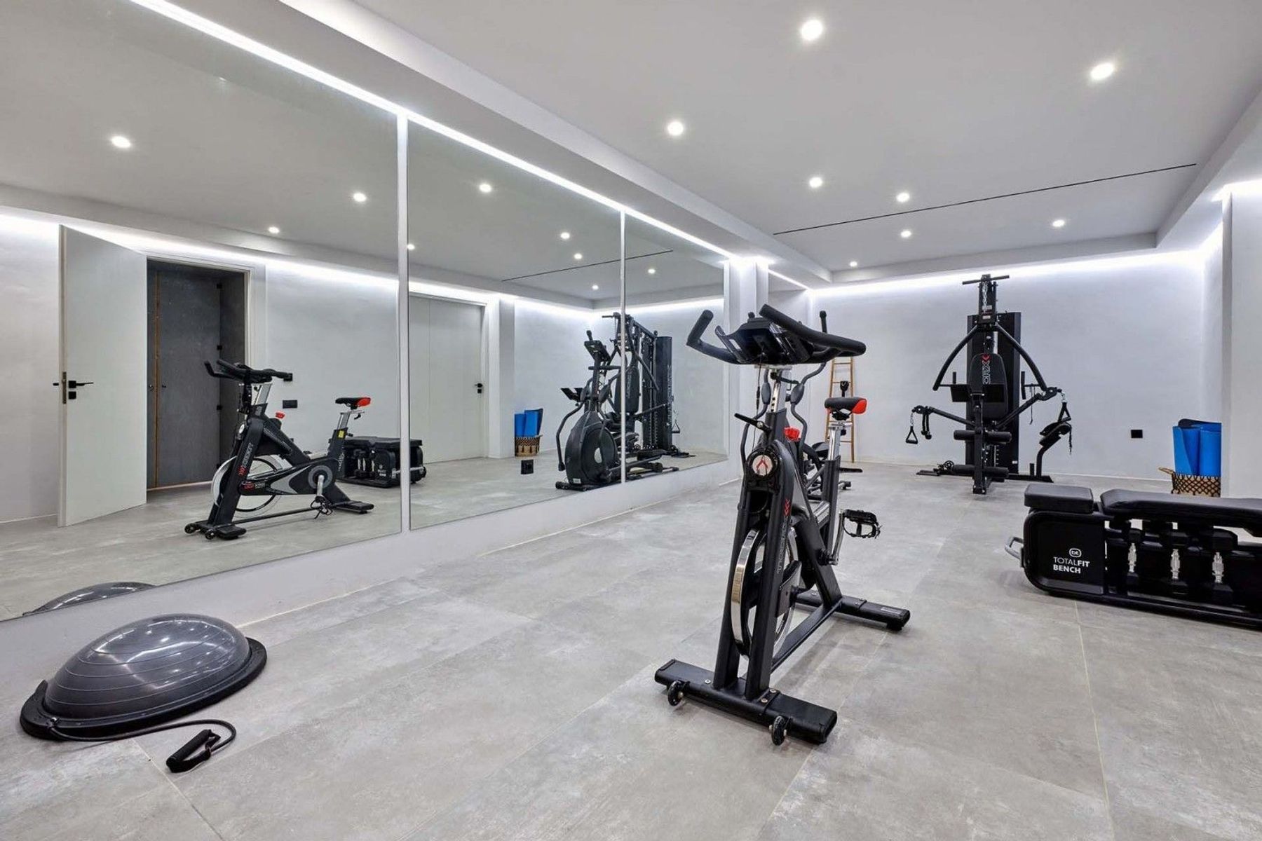 Private gym area with an elliptical trainer, spinning bike, weight station, dumbbells, and training balls.