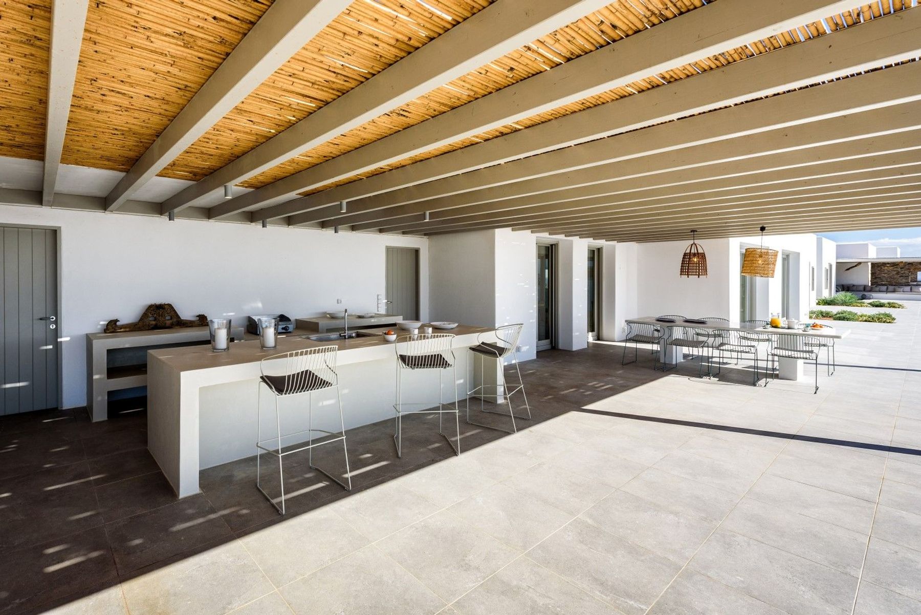 Outdoor shaded kitchen with bar area, and dining table seating eight guests.