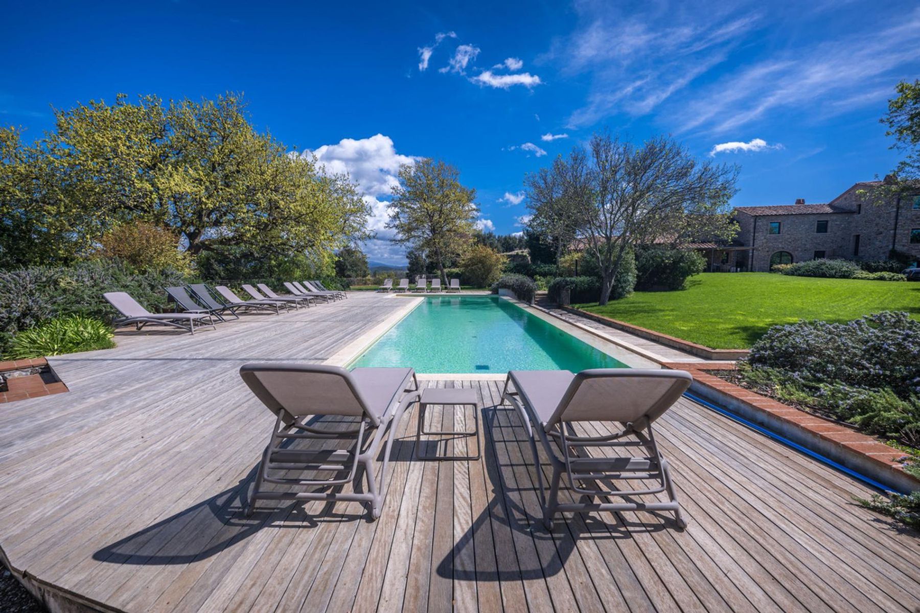 Shaded by ancient oak trees, a spacious wood deck surrounds the pool, flanked by sun beds.