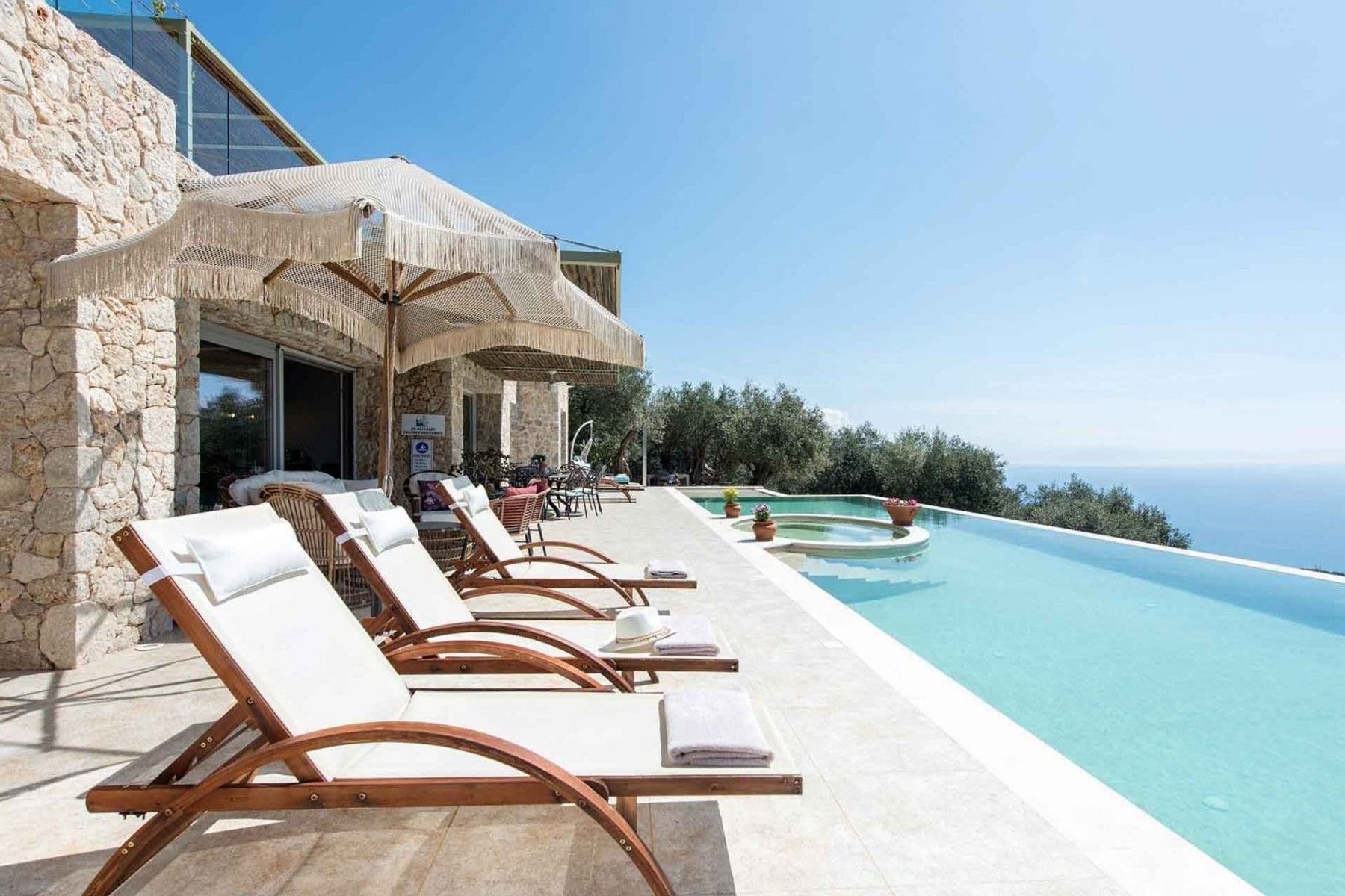 A stunning outdoor pool terrace with sun beds, parasols, and breathtaking views of the sea.